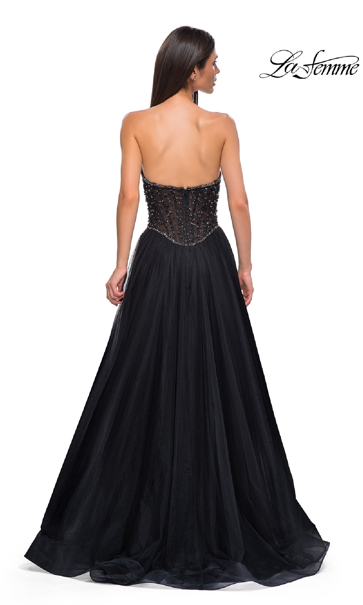 A woman stands with her back to the camera in the Strapless Long Black Prom Ball Gown: La Femme 32856, featuring a beaded bodice and full floor-length skirt against a plain white background.